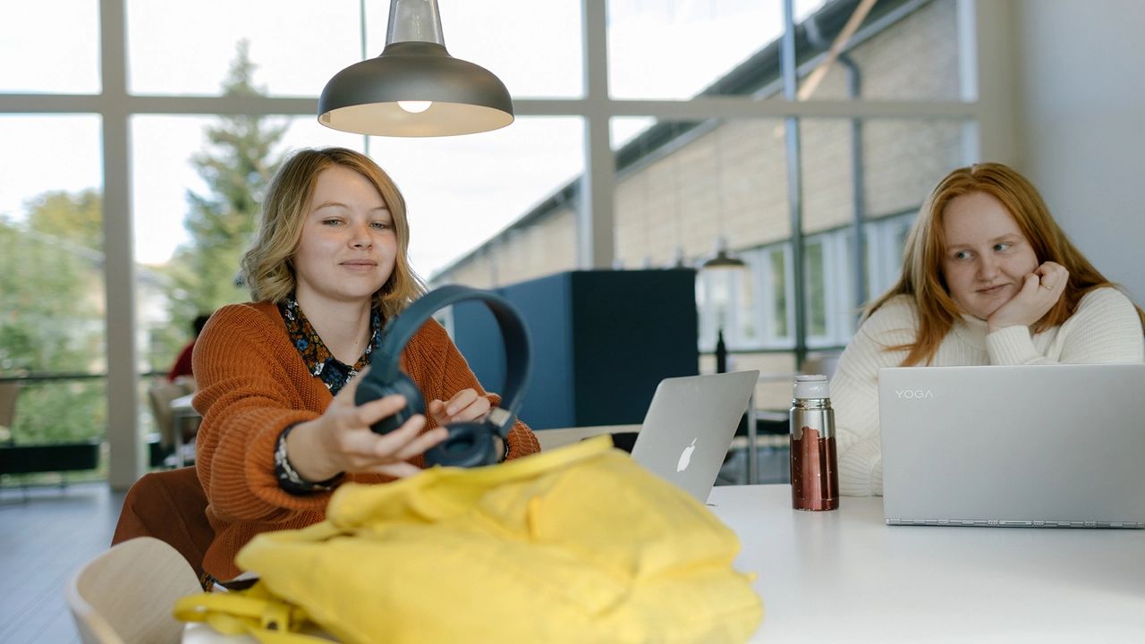 Två personer sitter vid ett bord med datorer. En person håller i hörlurar. Studenter på välkomstmässan.