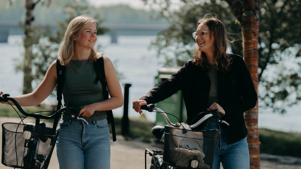 Two female students are walking their bikes to their student accommodation.