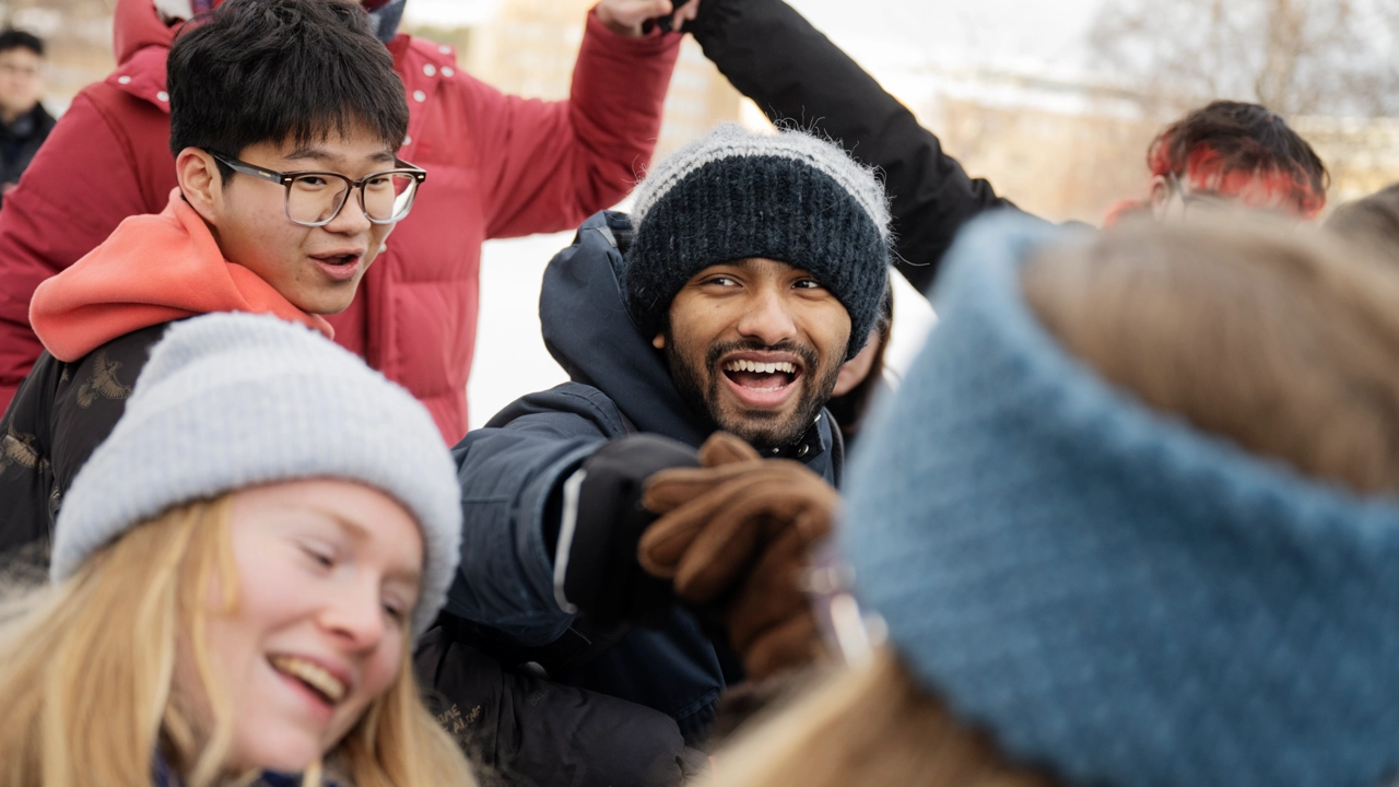 A group of smiling students with their arms together during a teambuilding activity in a snowy landscape.