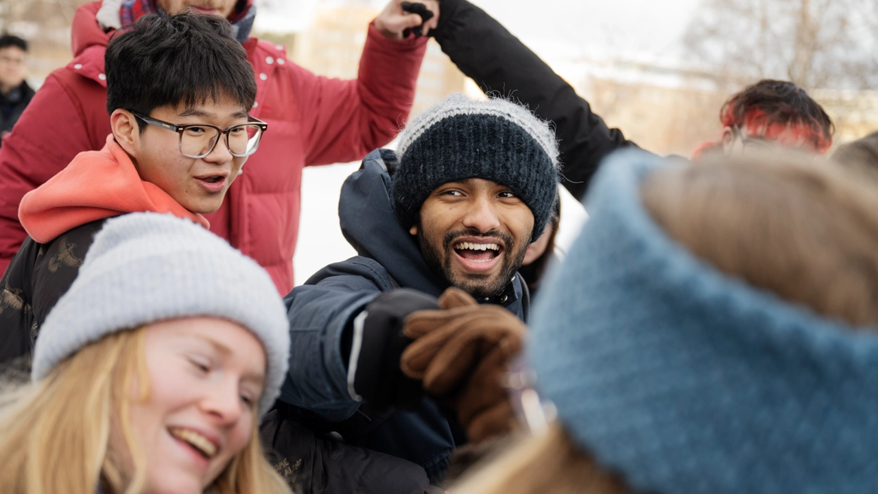 A group of laughing students engaged in a team activity in the winter landscape on campus.