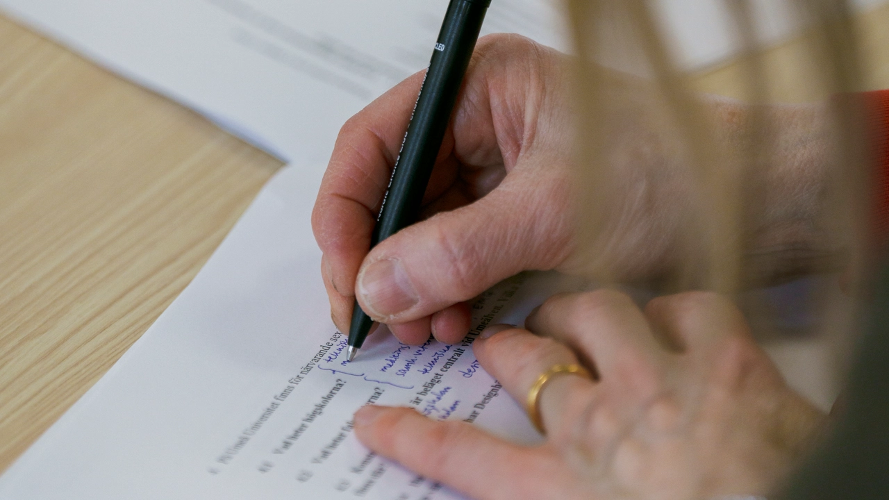 Två händer syns skriva på ett papper under ett prov.