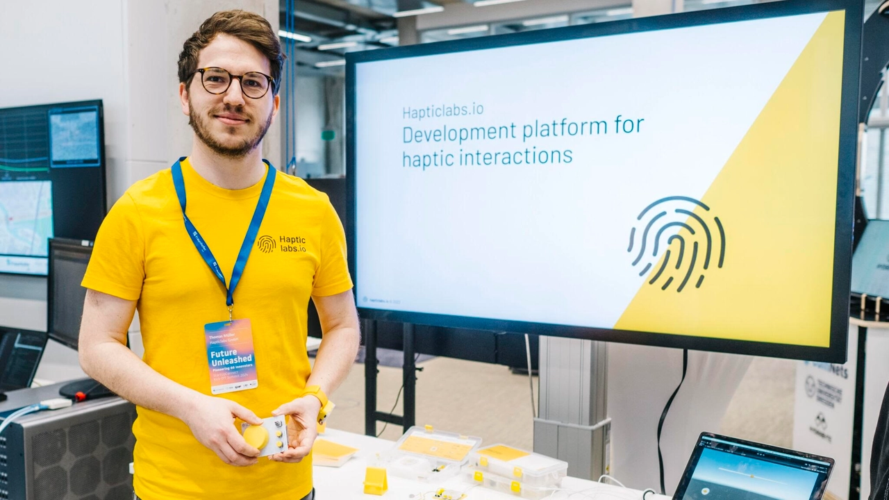 Photo of Thomas Müller standing next to large computer screen