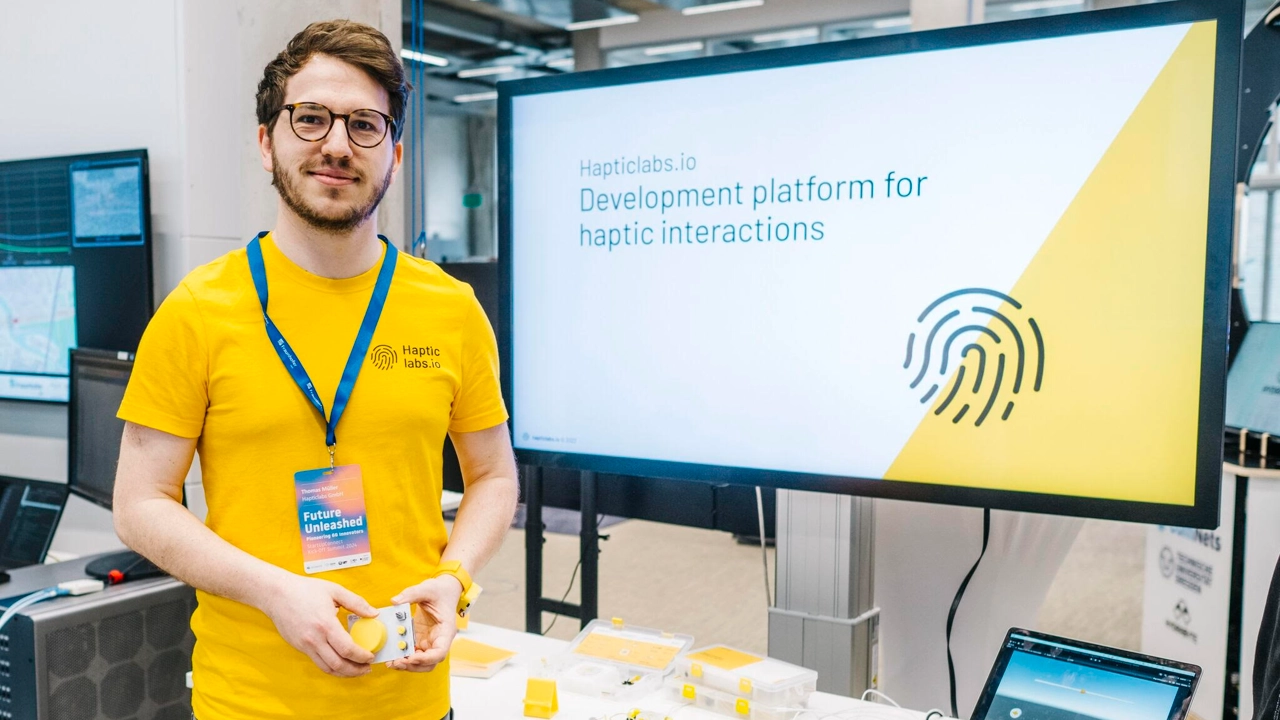 Photo of Thomas Müller standing next to large computer screen