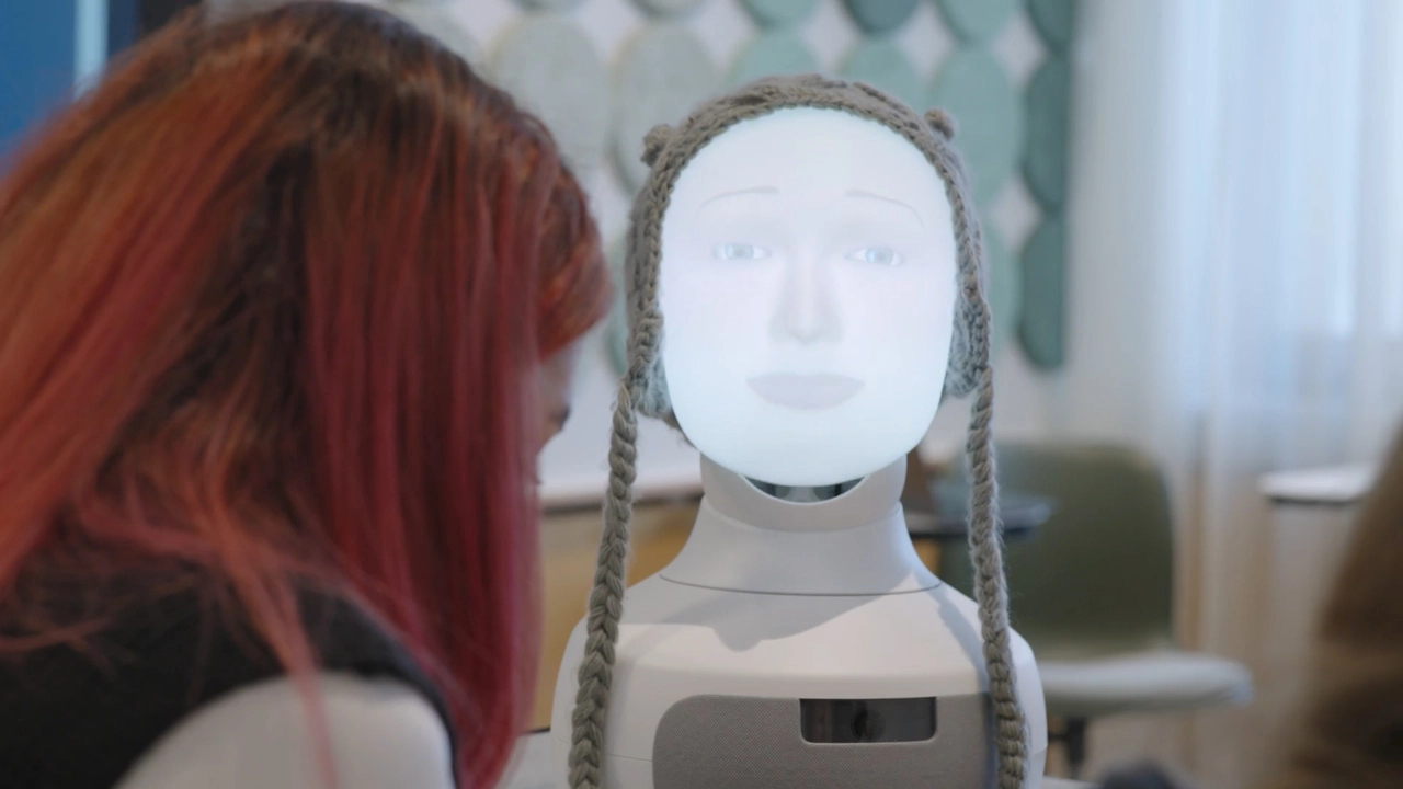 Foto av ett robotansikte med två människor som skymtar i förgrunden
