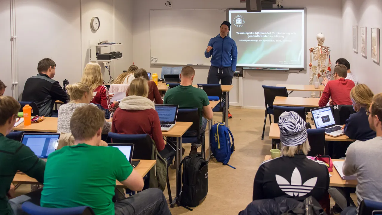 A classrom with students sitting with their back to the camera and a male teacher stood at the front.