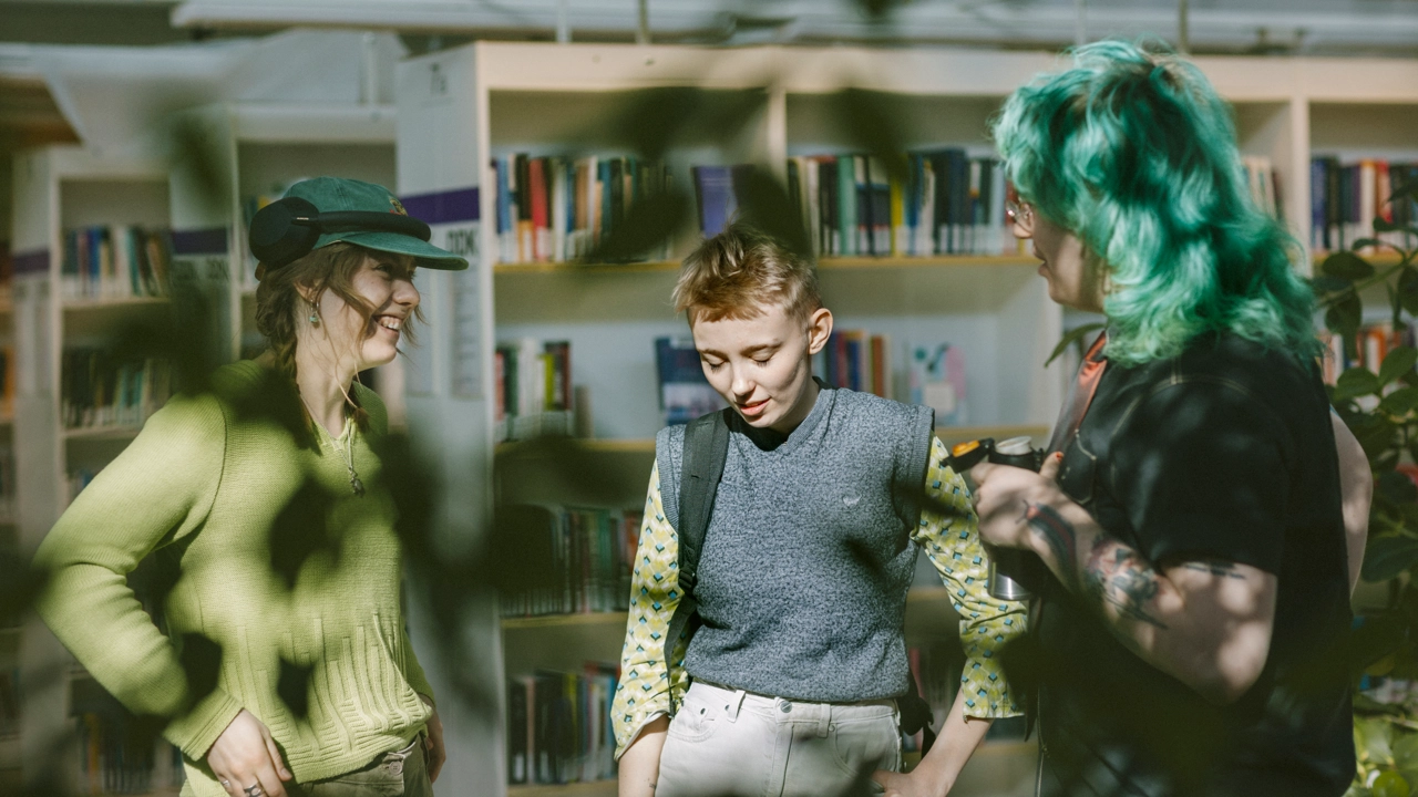 En grupp studenter står i en verkstad omgiven av verktyg och studentarbeten.