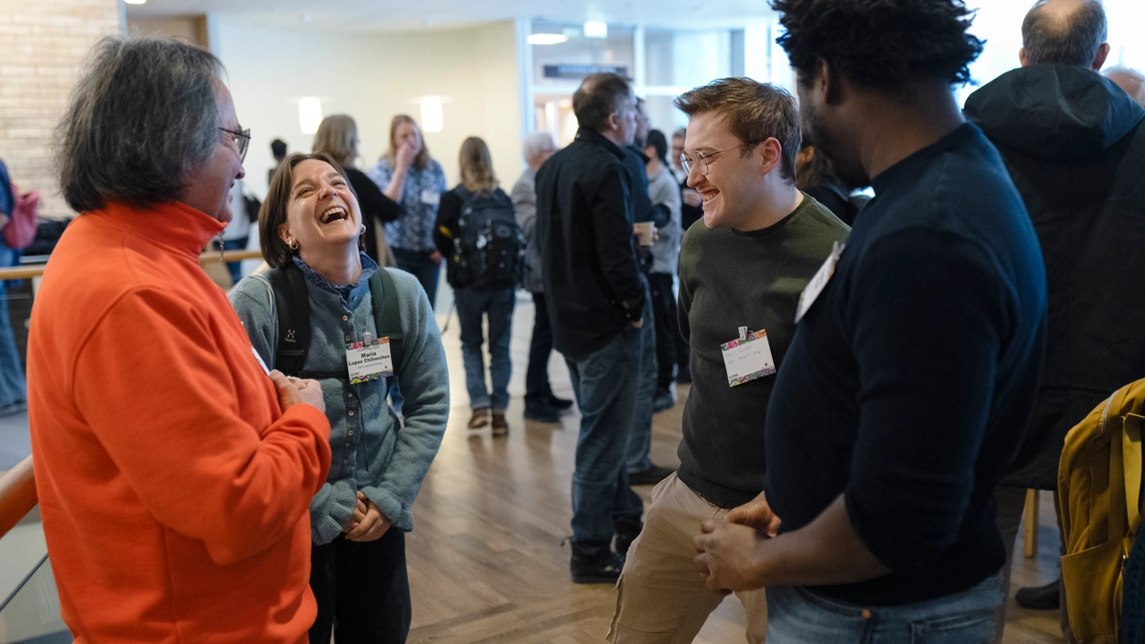 A group of conference participants laughing whilst people mingle in the background.