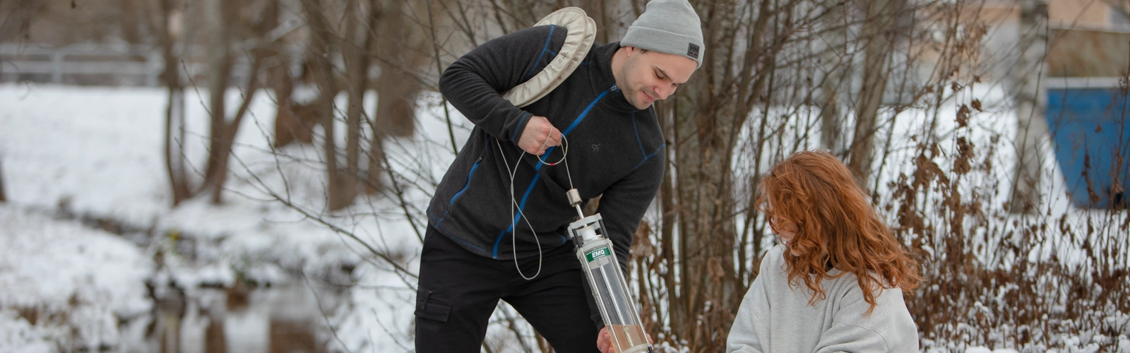 Två studenter med provtagningsutrustning tar prover på vattnet i bäcken på campus.