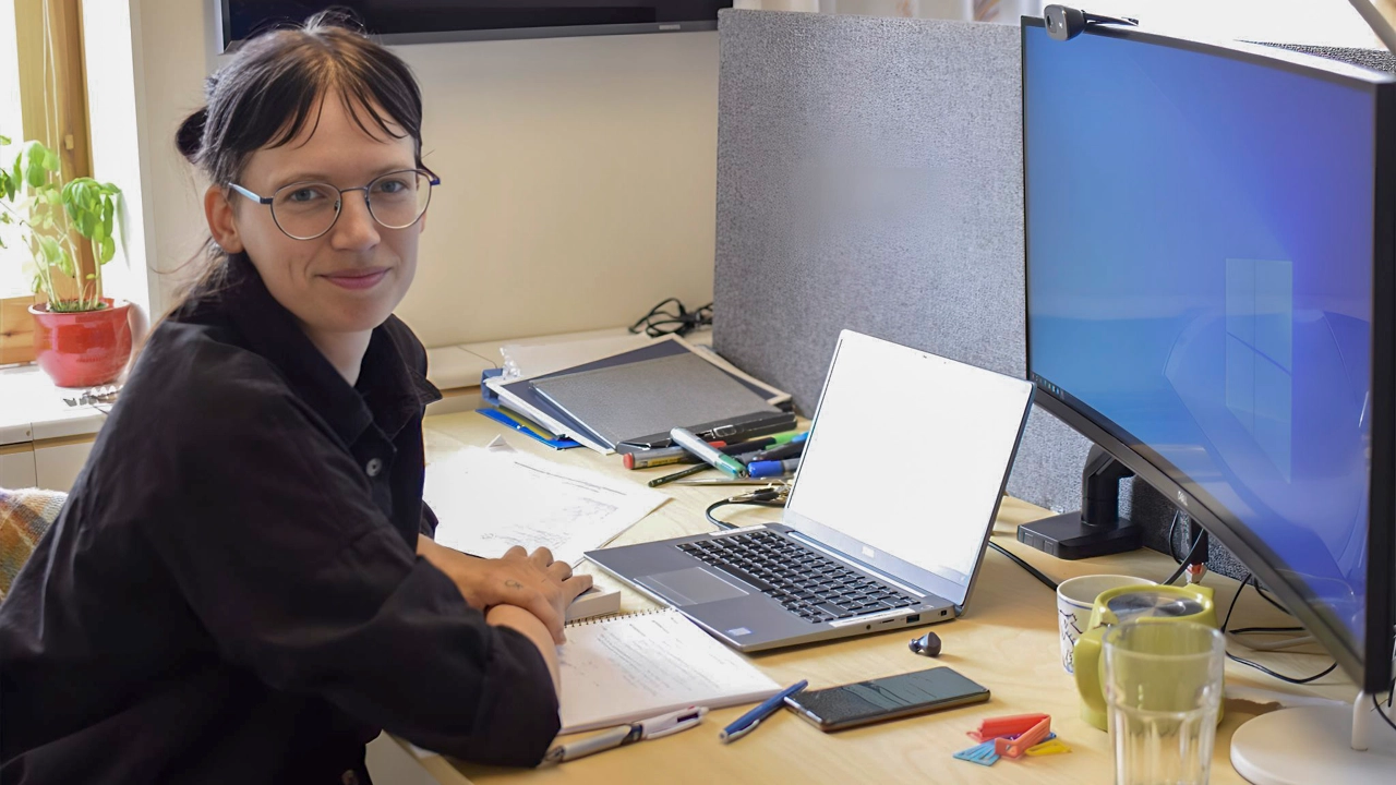 Bild på Willeke Martens sittande vid skrivbord med datorer framför sig