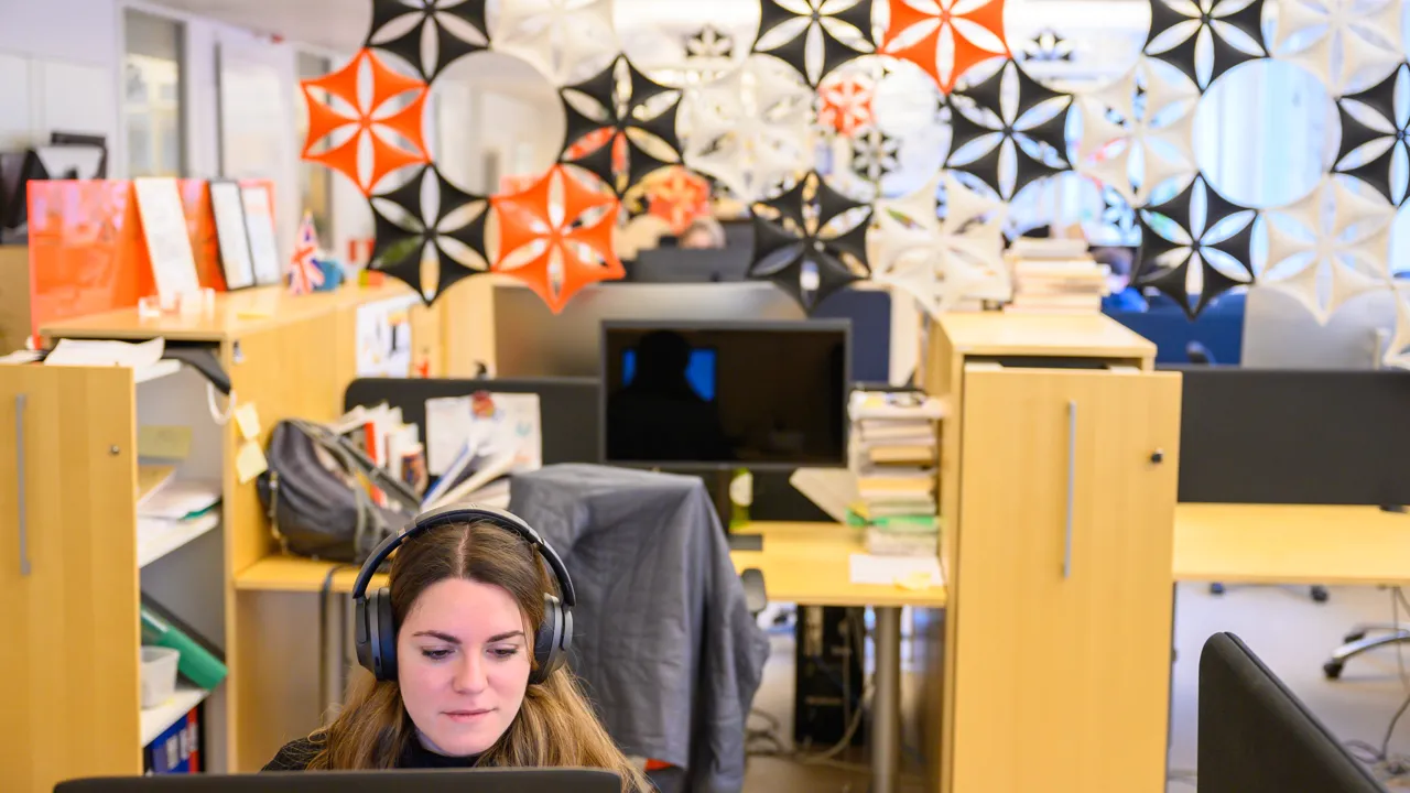 En kvinna sitter framför en bärbar dator med hörlurar på sig